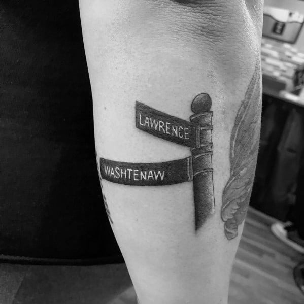 Black and grey tattoo of a classic street signpost featuring 'Lawrence' and 'Washtenaw' with realistic shading and fine details.