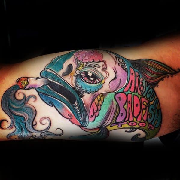 Whimsical tattoo of a colorful fish smoking, with exaggerated features and the phrase “Are You A Badfish Too?” in bold lettering.