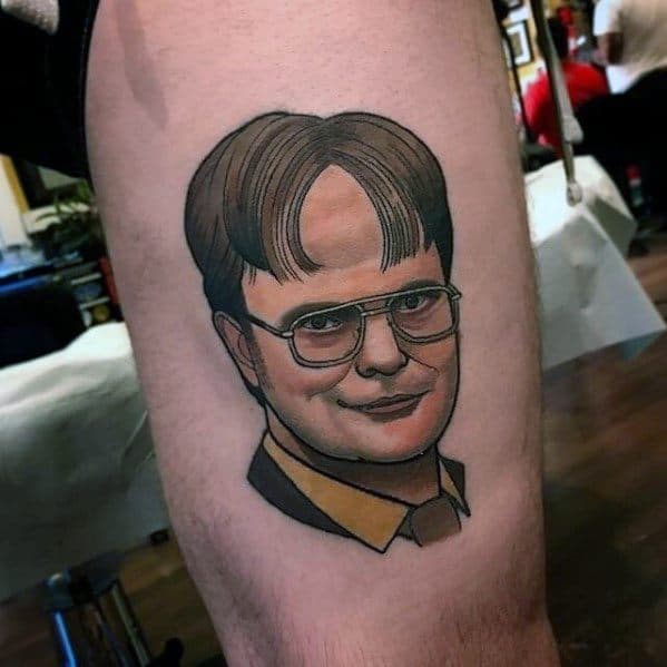 Color tattoo of Dwight Schrute from *The Office*, featuring his signature glasses, yellow shirt, and smug expression.
