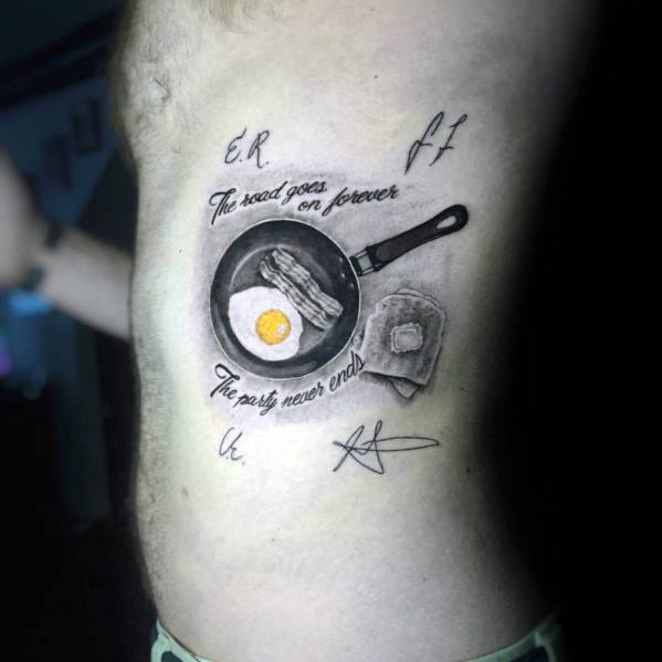 Realistic breakfast tattoo featuring a frying pan with bacon and eggs, a slice of toast, and the phrase "The road goes on forever, the party never ends."