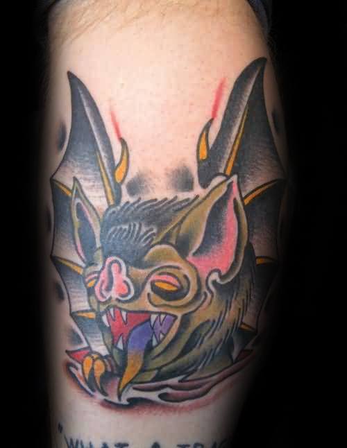 Traditional bat head tattoo with exaggerated yellow eyes, colorful tongue, sharp fangs, and bold shading in earthy tones.