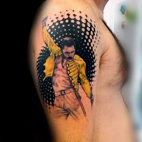 Colorful Freddie Mercury tattoo on the upper arm, showing his signature pose in a yellow jacket with a bold halftone dot background.