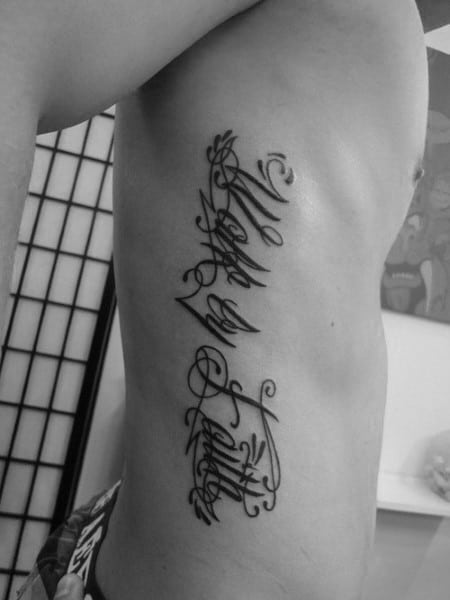 Rib tattoo featuring elegant cursive script running vertically along the side, creating a bold yet intricate statement on the body.