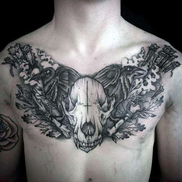 Chest tattoo of two birds, a skull, and floral designs on a person's upper chest