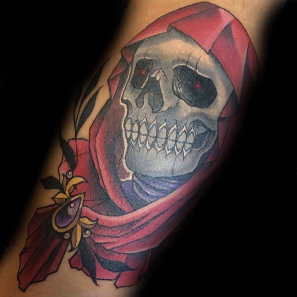 Color tattoo of a grinning skull in a red hooded cloak with glowing red eyes, holding a jeweled dagger with dark floral accents.