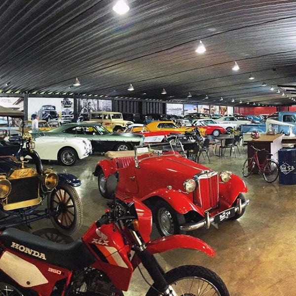 A massive dream garage showcasing a vast collection of classic cars and motorcycles under a sleek metallic ceiling.