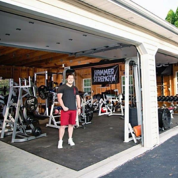 Spacious garage gym with multiple strength training machines, dumbbells, and open wooden interior.