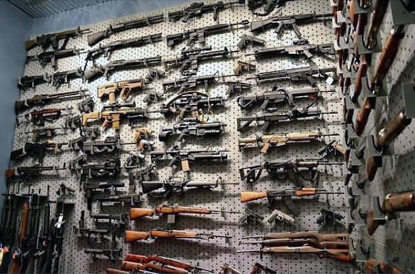 Gun room with an extensive pegboard wall displaying a large collection of rifles and firearms.