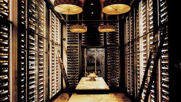 A dimly lit wine cellar with shelves of vintage wine and a marble table in the center