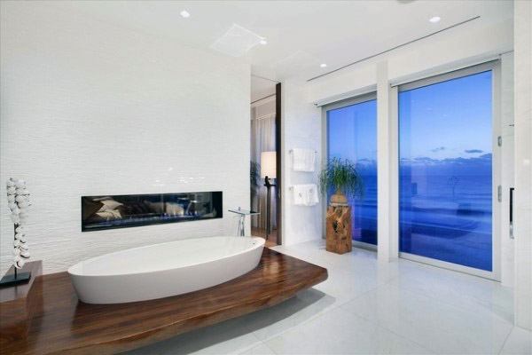 Modern bathroom with a freestanding tub, fireplace, and large window with an ocean view