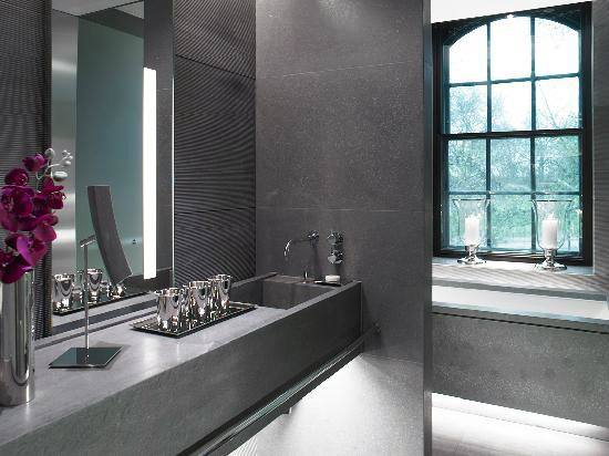 Modern bathroom with sleek dark vanity, illuminated mirror, and arched window with candles.