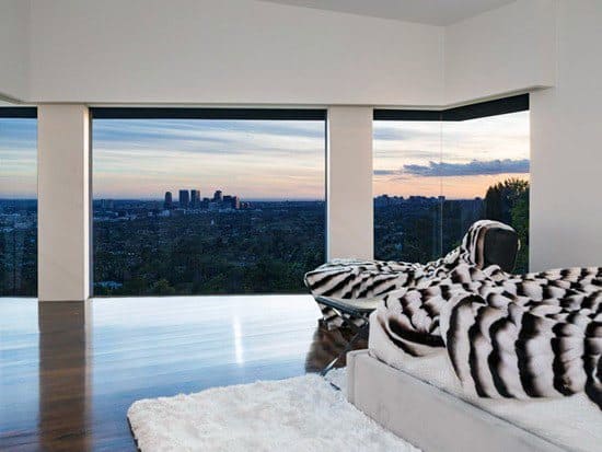 Luxury bedroom with panoramic city views, sleek decor, and a soft fur-patterned blanket.
