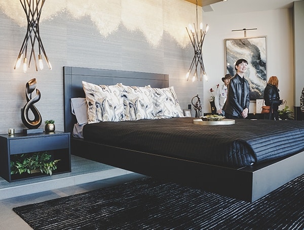 Modern bedroom with a black bed, abstract pillows, hanging lights, and art on the wall