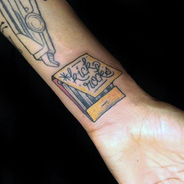Colorful matchbox tattoo on wrist with the phrase "kick rocks," blending playful defiance with a vintage design twist.