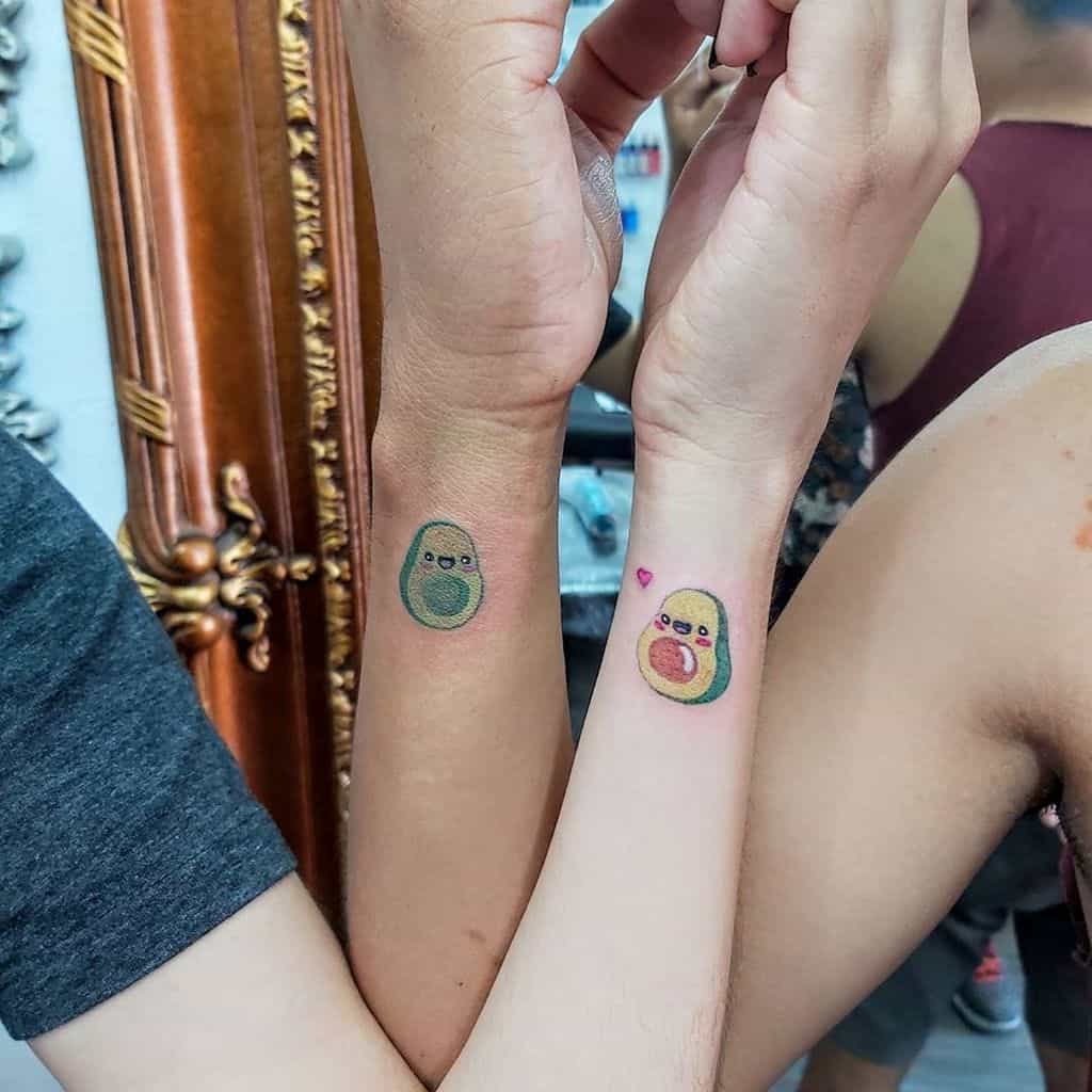 Two forearms displaying matching avocado cartoon tattoos; one half with a seed, the other with a small pink heart