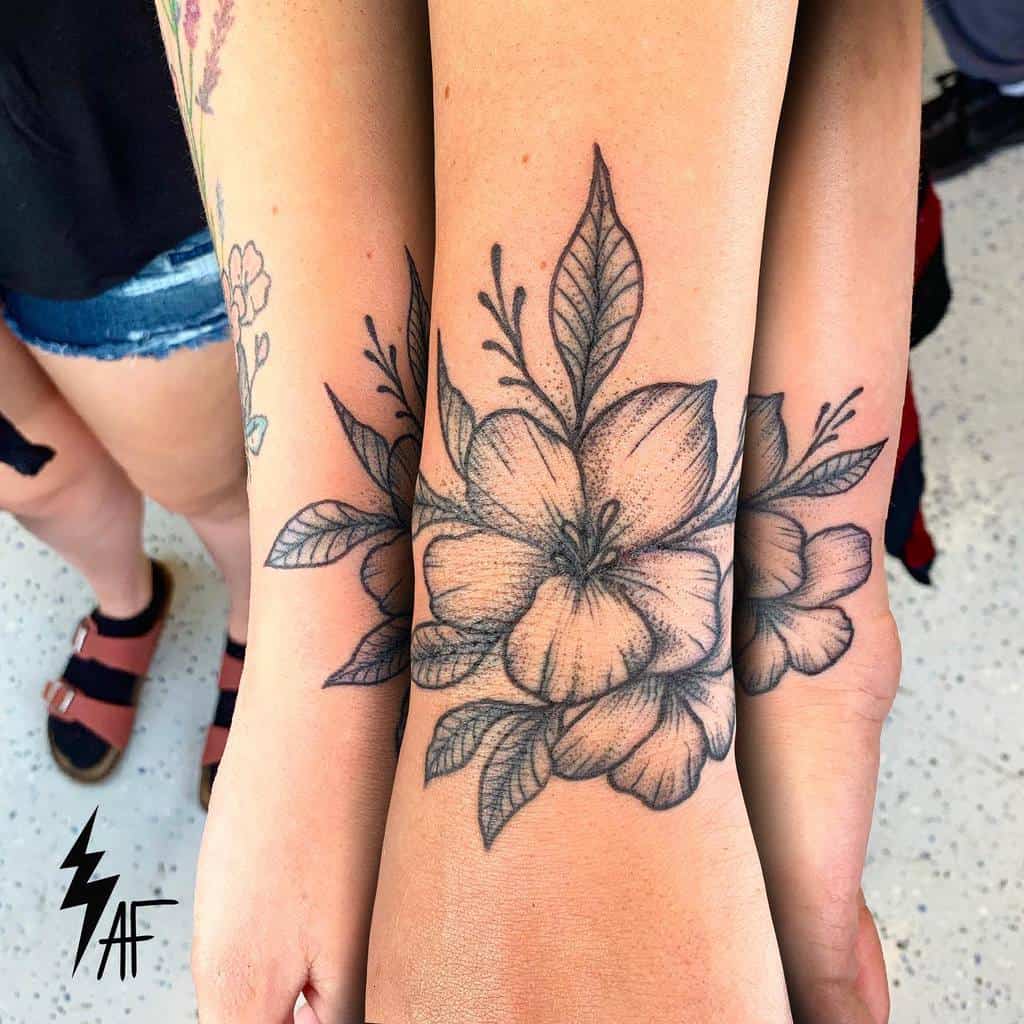 Matching black ink floral tattoos featuring large blooming flowers and leaves on the inner wrists of three individuals