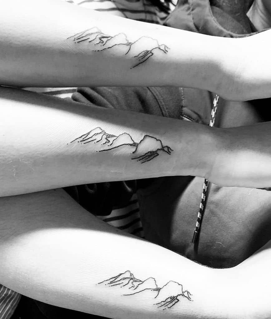 Matching sister sibling tattoos featuring minimalist mountain line art, symbolizing adventure, strength, and shared experiences