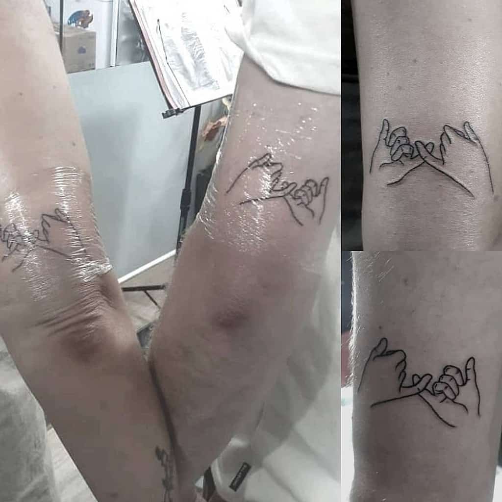 Matching tattoos of two hands making a pinky promise, shown freshly inked on forearms with clear protective wrap