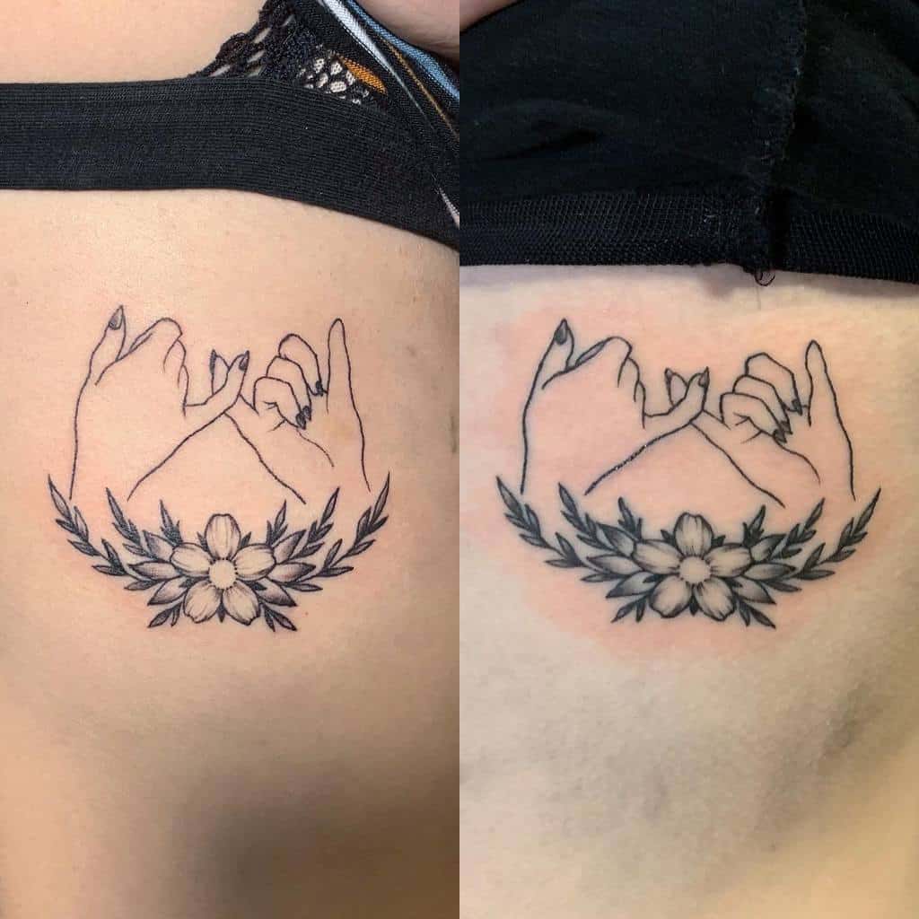 Tattoo of two hands making a pinky promise, surrounded by laurel branches and a flower at the bottom, in black ink