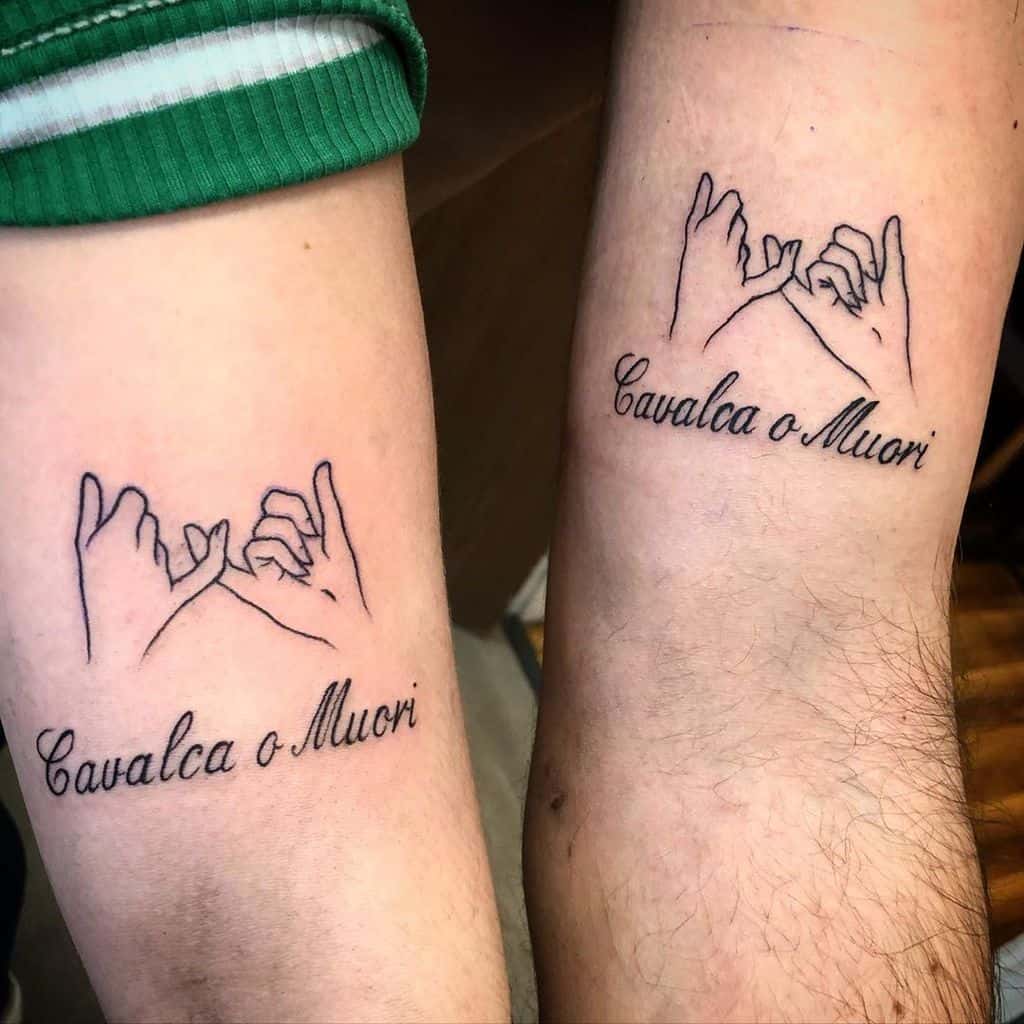 Two forearms with matching tattoos of intertwined pinky fingers and the phrase "Cavalca o Muori" below each