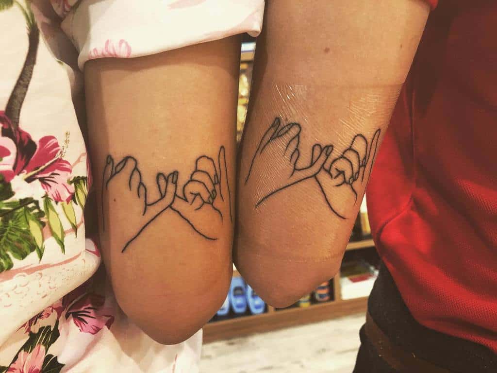 Two arms with matching pinky promise tattoos