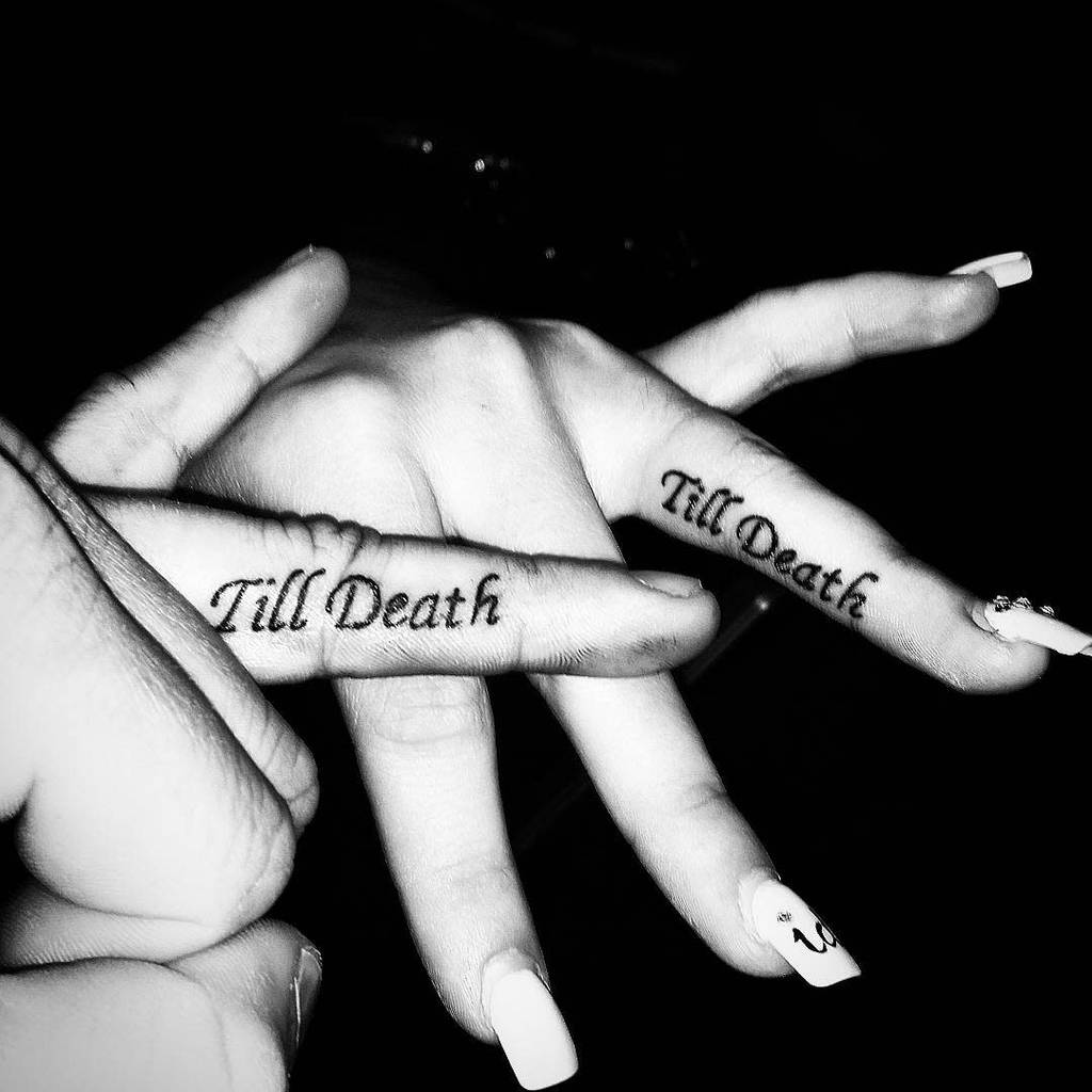 Matching wedding ring tattoos of the phrase "Till Death", symbolizing eternal commitment, in a black-and-white design