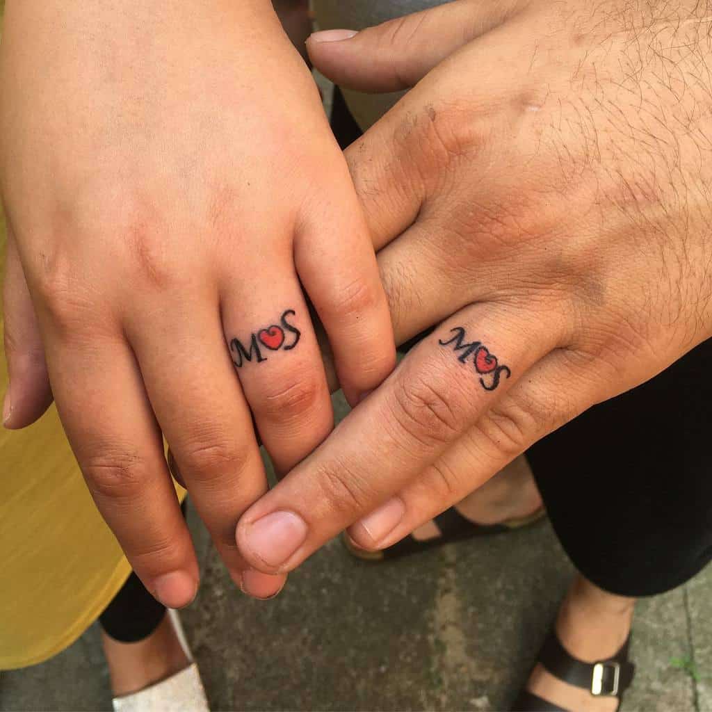 Matching wedding ring tattoos featuring the letters "S" and "M" with a heart in between, symbolizing love and connection