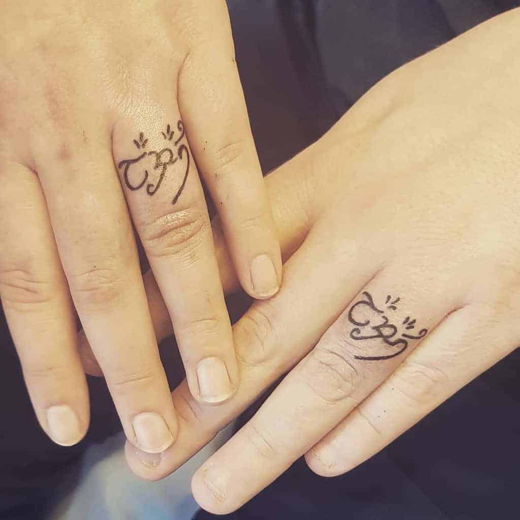 Two hands with matching Arabic calligraphy tattoos on their ring fingers