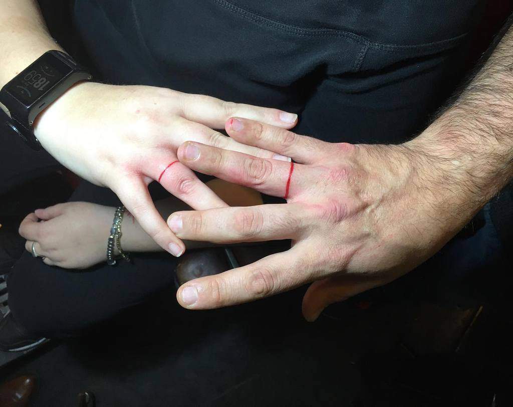 Matching minimalist red line wedding ring tattoos on the fingers, symbolizing connection or commitment