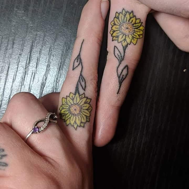 Inside middle fingers matching tiny color yellow daisies tattoos