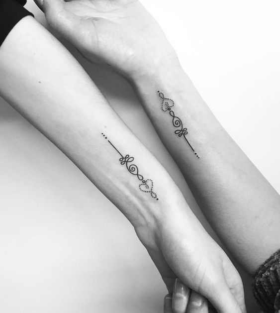Matching Unalome tattoos on wrists with heart details, symbolizing shared spiritual journeys, love, and personal growth.