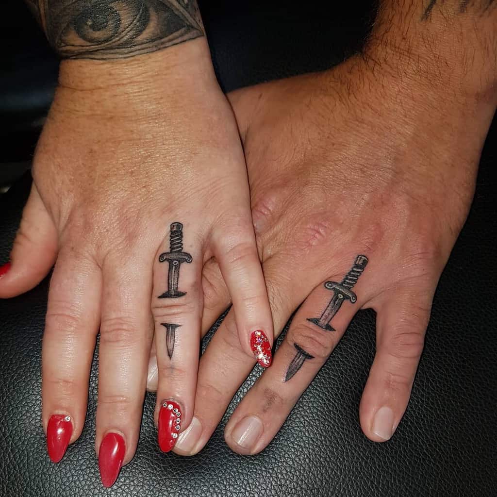Matching wedding ring tattoos of crossed swords on the fingers, symbolizing a deep connection or bond