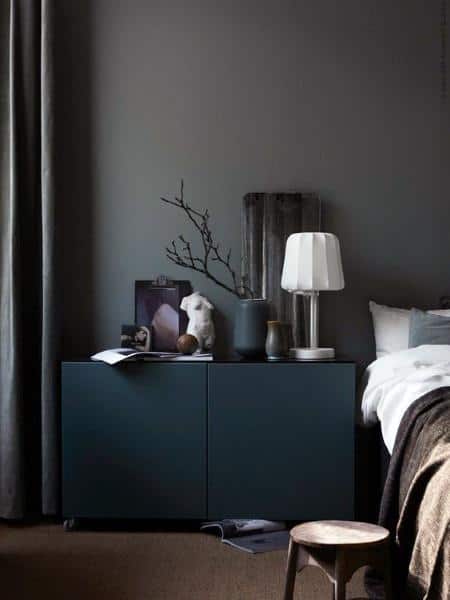 Modern bedroom with dark cabinet, decorative branches, table lamp, and minimalist decor.