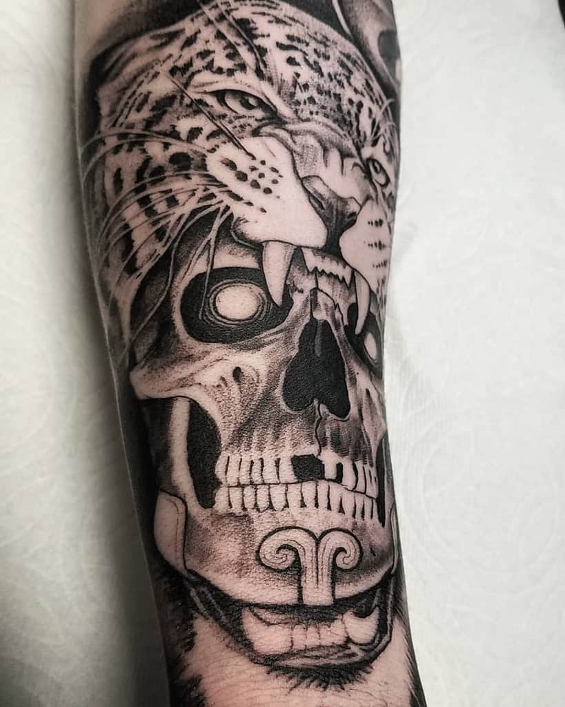 A powerful black and grey tattoo of a jaguar seemingly devouring a skull, with intense shading and detailed features on the forearm.