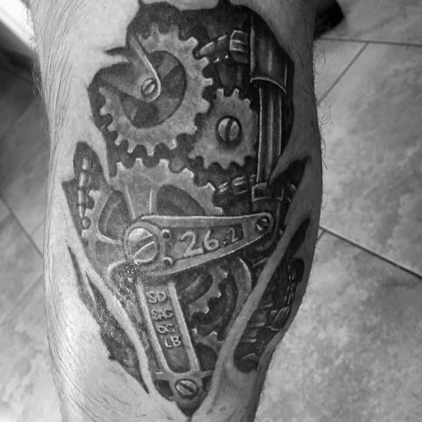 Mechanical-style tattoo with exposed gears and “26.2” engraved on a crank, symbolizing the inner drive and endurance of a marathon runner.