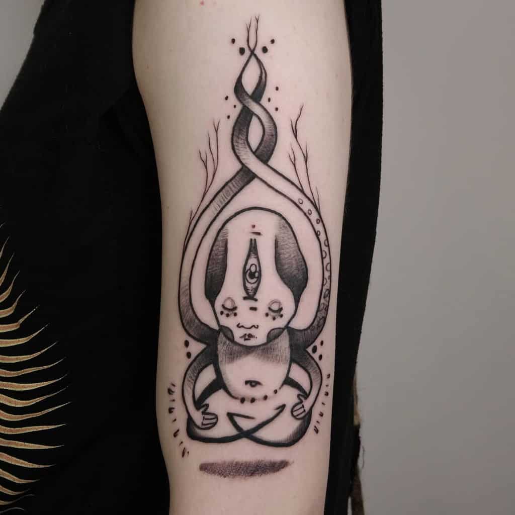 Tattoo of a meditating figure with a third eye, surrounded by twisting organic shapes, inked in black with dot shading on the upper arm.
