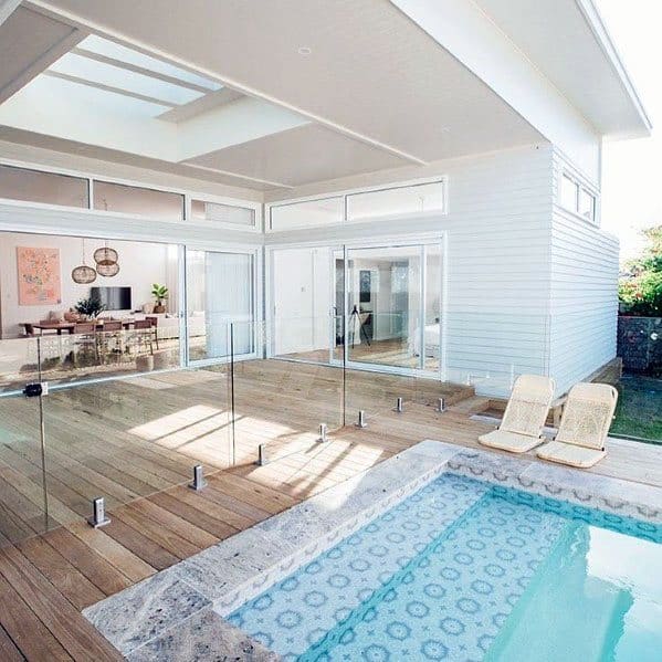 Mediterranean-style pool with patterned tiles, wooden deck, and sleek glass fencing.