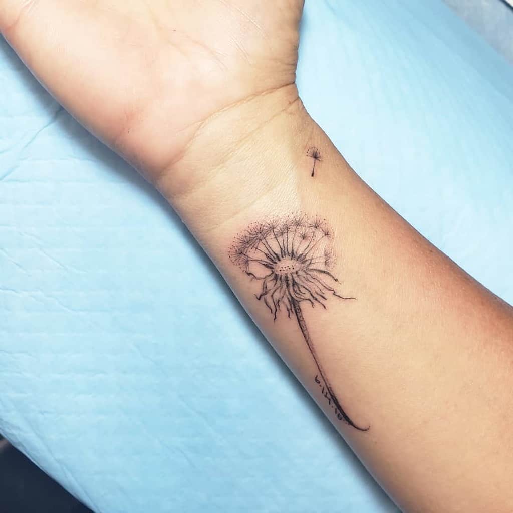 Fine-line dandelion tattoo on the wrist with seeds blowing away, symbolizing hope, freedom, and new beginnings.