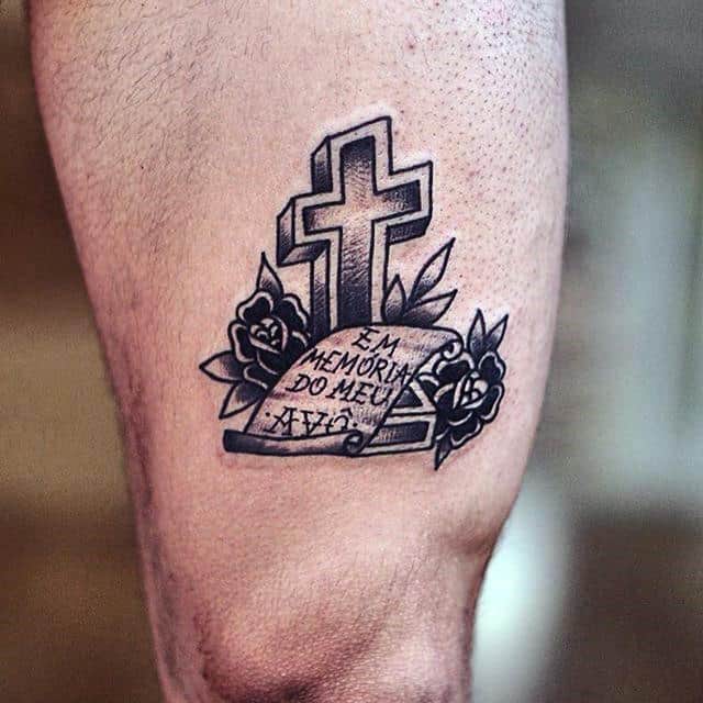 Tattoo of a cross and roses with text "Em memória do meu avô" on a leg