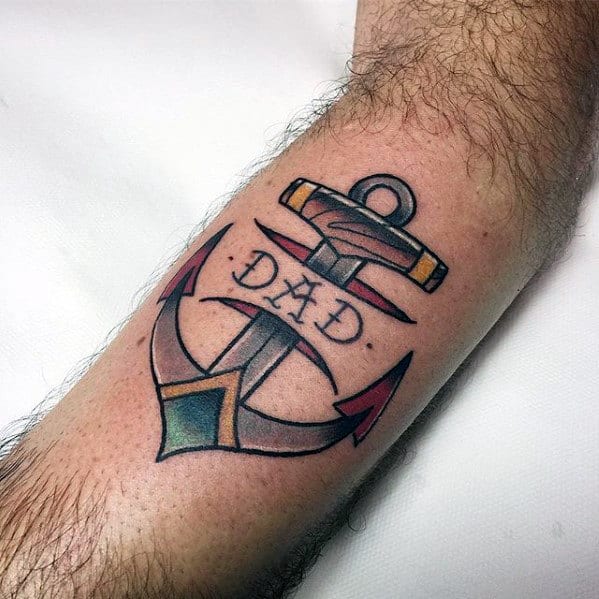 Traditional anchor tattoo with "Dad" inscription, bold black outlines, red arrow tips, and subtle shading, symbolizing strength and tribute.