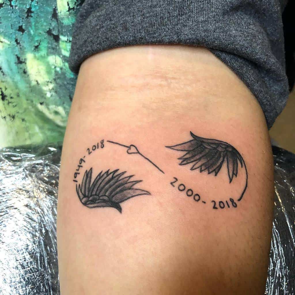 Tattoo of angel wings forming an infinity symbol with dates "1949-2018" and "2000-2018" connected by a heart