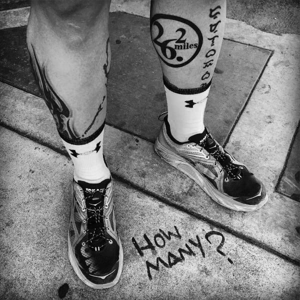 Bold 26.2 miles tattoo inside a circular arrow with tally marks and “How many?” on the ground, celebrating repeated marathon achievements.