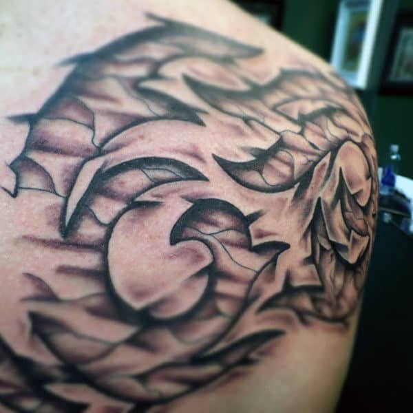 Abstract black and grey tribal tattoo design on a person's shoulder, featuring curving lines and sharp edges