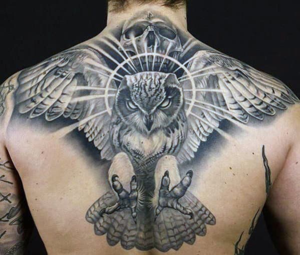 Back tattoo of an owl with wings spread and talons extended, set against a dark background