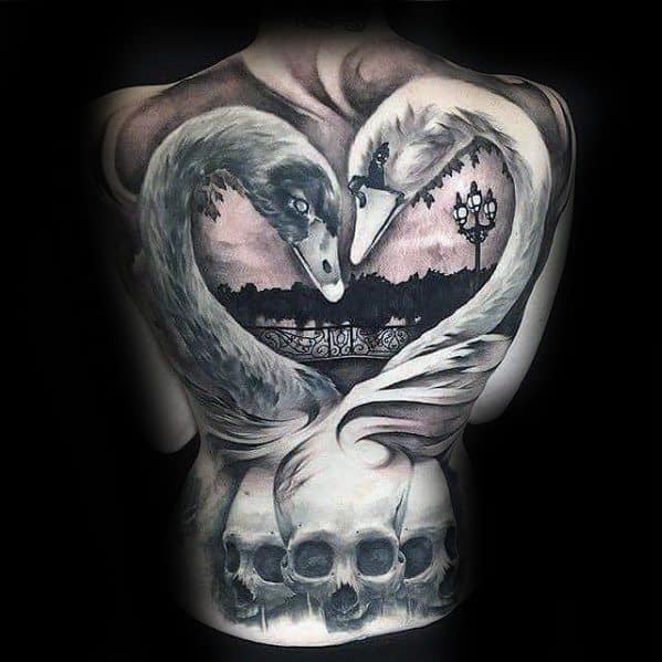 Full back tattoo of two swans forming a heart shape, set against a romantic cityscape and lamp post, with skulls below adding a dark twist.