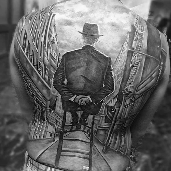 Large back tattoo featuring a man in a suit and hat sitting on a chair in the middle of a surreal cityscape with distorted buildings.