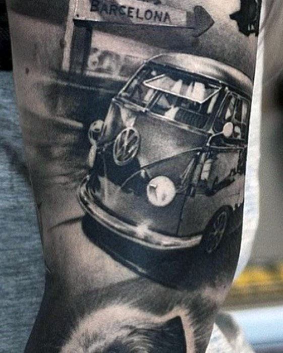 Realistic black and gray tattoo of a Volkswagen van with a directional sign pointing to Barcelona in the background.