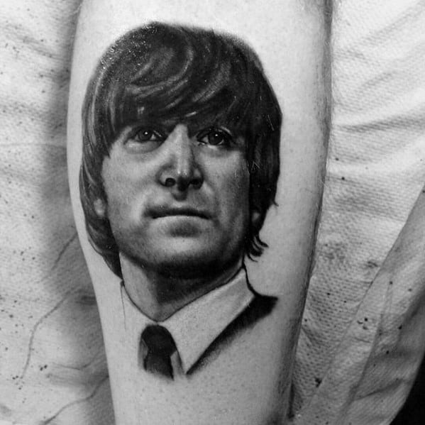 Realistic black and gray portrait tattoo of a young John Lennon in a suit and tie, capturing his early Beatles-era look with detailed shading.