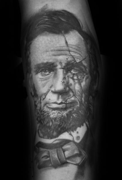 Black and gray tattoo of Abraham Lincoln with a beard and bow tie on an arm