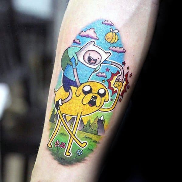 Adventure Time tattoo of Finn riding Jake through a colorful landscape, holding a sword with lightning, inked on the inner forearm.
